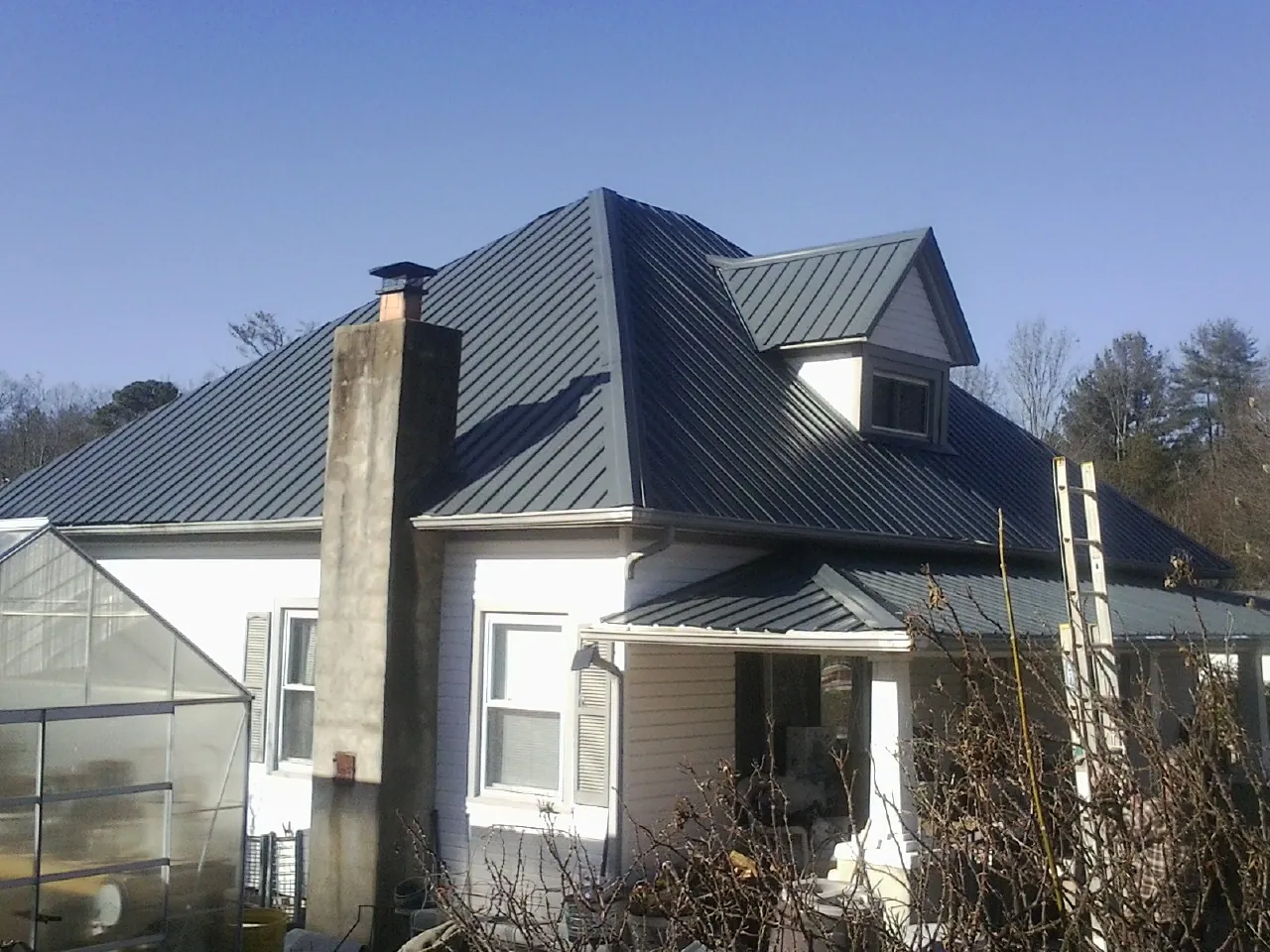 Dark blue standing seam metal roof on a white farmhouse with dormer — Slate & Tile Roof Repair by Roofing Brothers in Eggleston