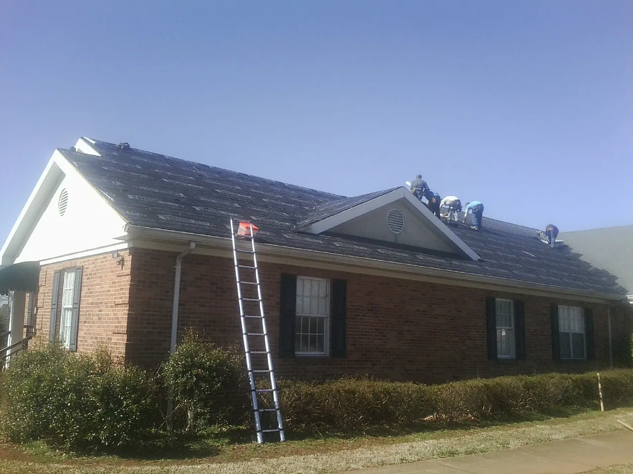 Crew tearing shingles off a brick ranch roof with a ladder set — Metal Roof Repair work by our crew in Eggleston