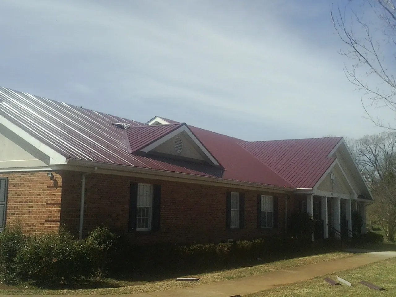 Red metal roof with gabled entries on a long brick building, from a Hail Damage Roof Repair job in Eggleston