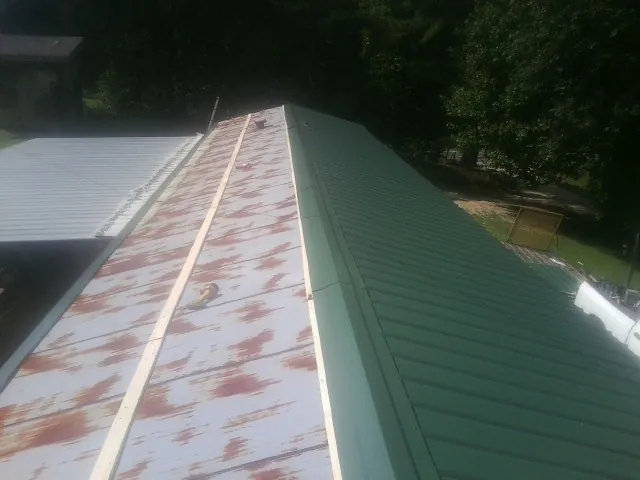 Old rusted panels beside newly installed green metal roofing — Wind Damage Roof Repair by Roofing Brothers in Eggleston