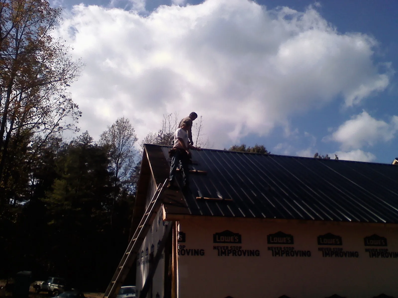 Roofer fastening dark metal panels high against a cloudy sky, from a Roof Inspection job in Eggleston